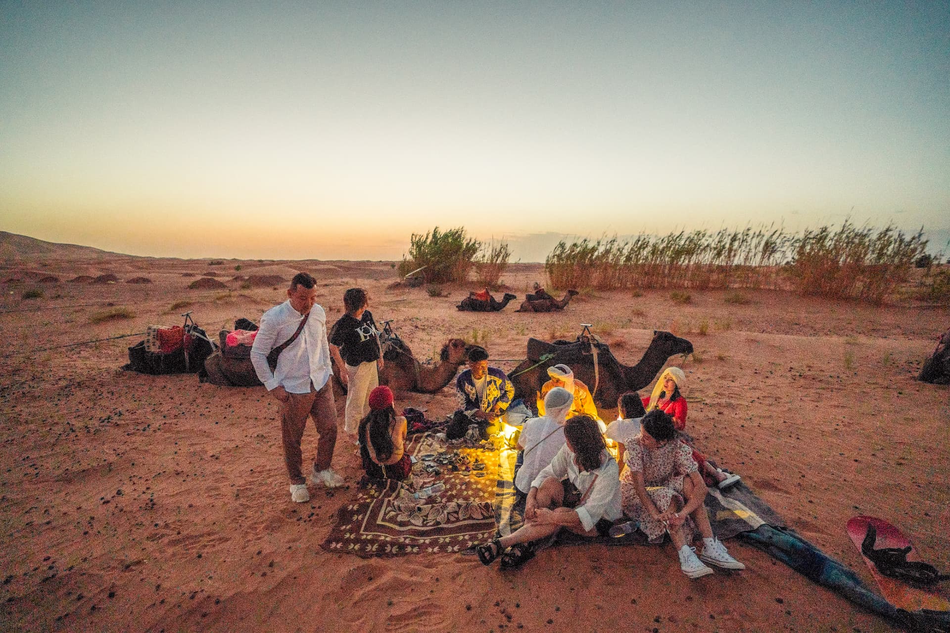 Travellers sharing a sunset picnic beside their camels in the Sahara